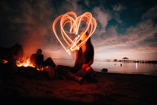 A woman is making a heart with sparklers as the evening sky darkens behind her